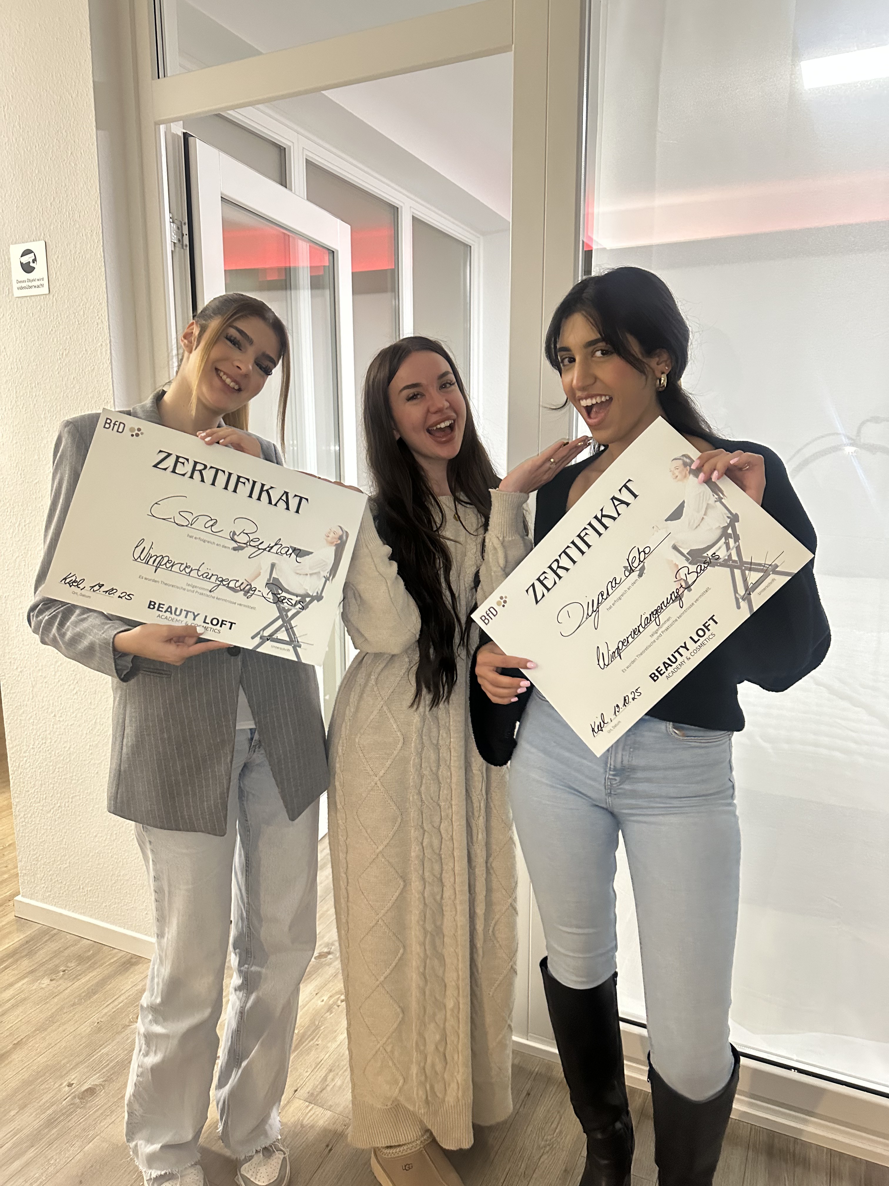 Drei Absolventinnen feiern ihre Zertifikate